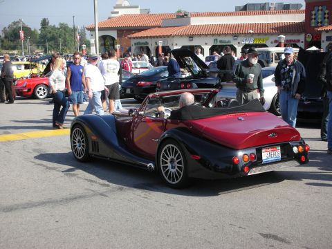1998 Ford Crown Victoria - maroon-and-black Morgan Aero-style roadster is shown from the rear three-quarter as people walk around it at a car show.