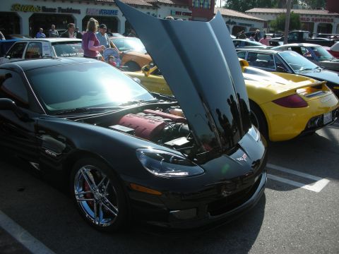 1998 Ford Crown Victoria - black Chevrolet Corvette Z06 displays its engine with the hood up, parked next to a yellow Porsche Carrera GT.