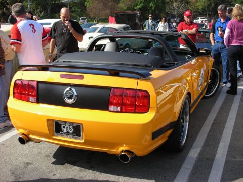 1998 Ford Crown Victoria - orange Ford Mustang convertible is shown from the rear with a black trunk panel and dual exhausts as onlookers gather.