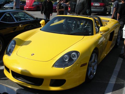 1998 Ford Crown Victoria - bright yellow Porsche Carrera GT roadster sits parked on asphalt at a car gathering, viewed from the front three-quarter angle.