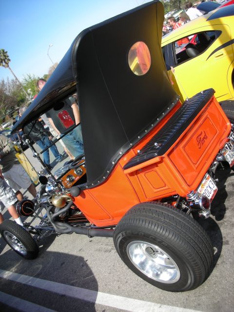 1998 Ford Crown Victoria - Rear three-quarter view of an orange Ford T-bucket with a black folding top, Ford-script bed and wide rear tire.