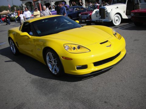 1998 Ford Crown Victoria - yellow Chevrolet Corvette Z06 C6 with chrome wheels is parked on asphalt with show cars and people behind it.