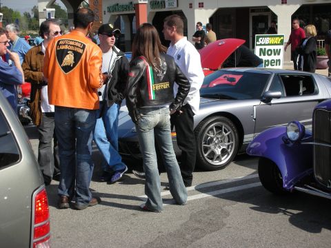 1998 Ford Crown Victoria - group chats at a car show, two wearing Automobili Lamborghini and Ferrari jackets, with a silver Ford GT behind them.
