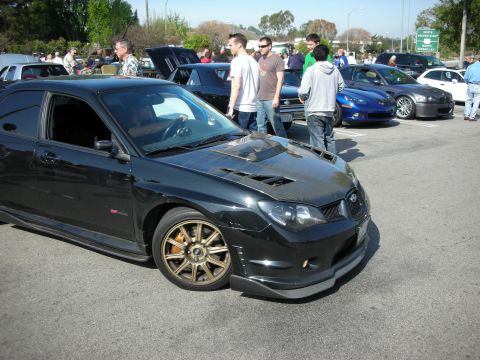 1998 Ford Crown Victoria - black Subaru Impreza WRX STI with hood scoop and gold wheels is parked among other cars at an outdoor show.