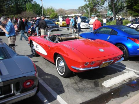 1998 Ford Crown Victoria - red early Chevrolet Corvette C1 convertible with chrome trim is parked beside a blue coupe at a sunny car gathering.