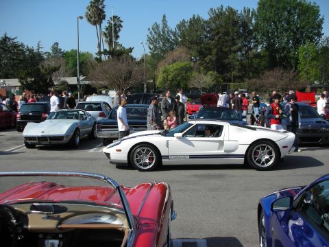 1998 Ford Crown Victoria - white Ford GT with blue racing stripes sits in profile among Corvettes and show cars on a sunny day.
