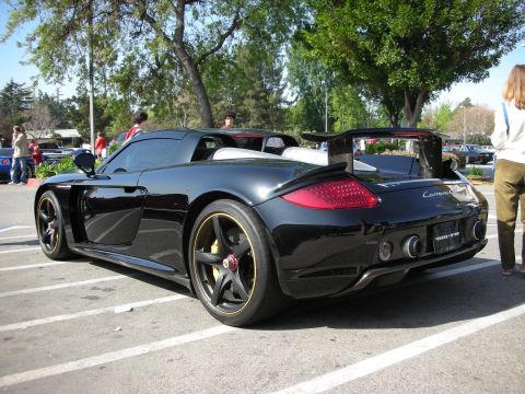 1998 Ford Crown Victoria - Rear three-quarter view of a black Porsche Carrera GT with gold wheels and raised spoiler parked at a car show.