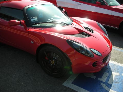1998 Ford Crown Victoria - red Lotus Elise with black wheels and engine intake vents is parked in a blue-striped accessible spot beside another red car.