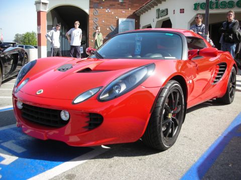 1998 Ford Crown Victoria - Front three-quarter view of a red Lotus Elise with black wheels parked outside a rotisserie storefront as people look on.