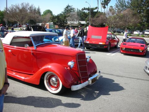 1998 Ford Crown Victoria - red 1930s Ford convertible hot rod with whitewall tires parked beside red Ferraris at an outdoor car meet.
