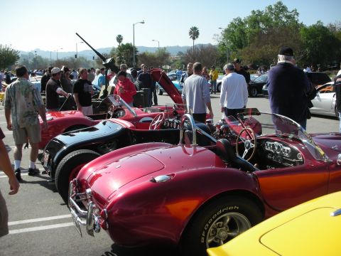 1998 Ford Crown Victoria - line of Shelby Cobra-style roadsters in red and black with people browsing the outdoor car show.
