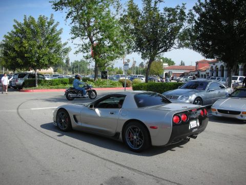 1998 Ford Crown Victoria - silver C5 Corvette coupe with dark wheels parked in a lot as a motorcyclist rides past.