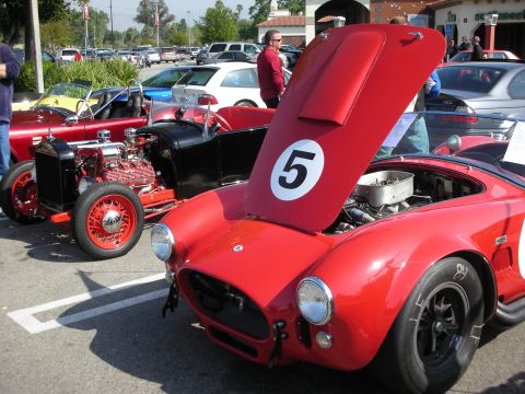 1998 Ford Crown Victoria - red Shelby Cobra roadster with its hood raised showing the engine and a number 5 roundel, beside a hot rod.