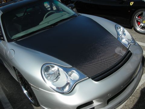 1998 Ford Crown Victoria - silver Porsche 911 with a bare carbon-fiber hood parked next to a black Ferrari at an outdoor show.
