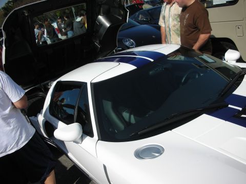 1998 Ford Crown Victoria - white Ford GT with blue racing stripes and its rear clamshell raised, surrounded by onlookers at a meet.