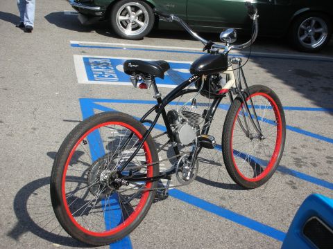 1998 Ford Crown Victoria - black motorized beach-cruiser bicycle with red-rimmed wheels parked over blue handicap-spot markings.