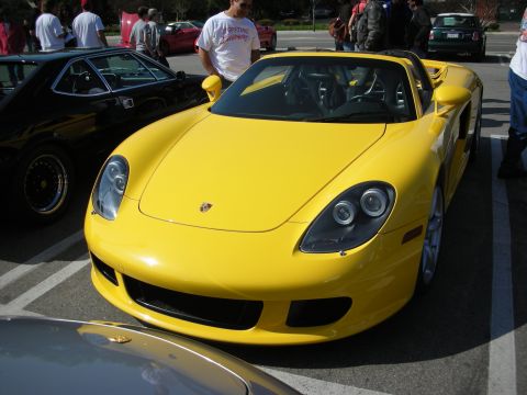 1998 Ford Crown Victoria - yellow Porsche Carrera GT parked front-on in a lot beside a black classic Porsche at a car gathering.