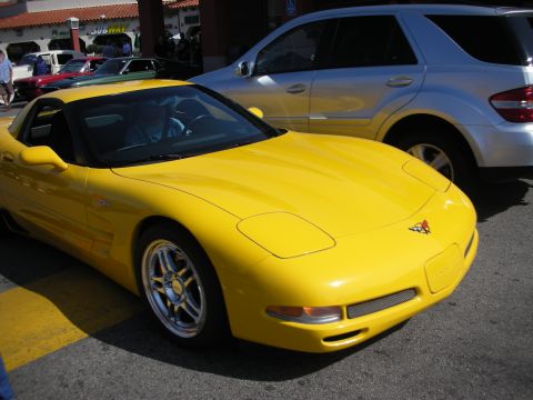 1998 Ford Crown Victoria - yellow Chevrolet Corvette coupe sits in a parking lot beside a silver SUV at an outdoor car show.