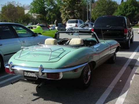 1998 Ford Crown Victoria - green Jaguar E-Type convertible with wire wheels and sheepskin seat covers seen from the rear in a parking lot.