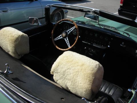 1998 Ford Crown Victoria - cockpit of a green Jaguar convertible showing a wood-rimmed steering wheel and cream fleece seat covers.