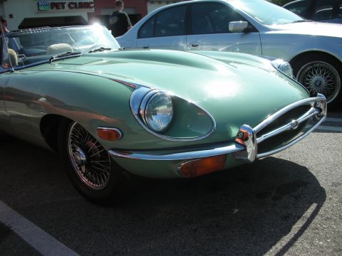 1998 Ford Crown Victoria - Close-up of a green Jaguar E-Type front fender, chrome bumper and exposed headlight with a chrome wire wheel.