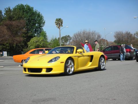 1998 Ford Crown Victoria - yellow Porsche Carrera GT open-top supercar sits in a parking lot among other cars at a car meet.