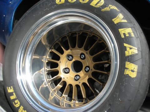 1998 Ford Crown Victoria - Close-up of a gold mesh center-lock racing wheel wrapped in a Goodyear Eagle slick tire on a blue car.