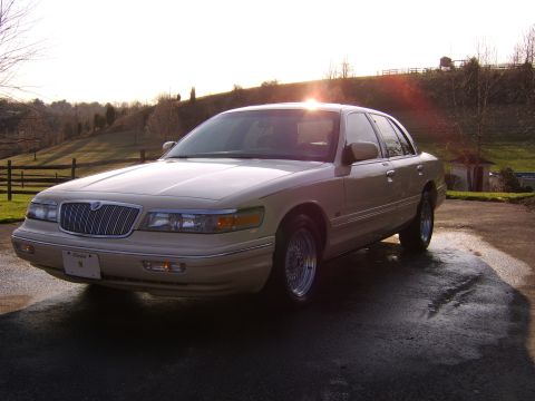 1996 Mercury Grand Marquis - A cream-colored sedan is parked outside on a sunny day, with a rural landscape in the background.