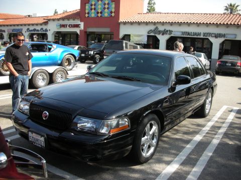1998 Ford Crown Victoria - black Mercury Marauder sedan with chrome wheels parked at a car meet in front of a shopping plaza.