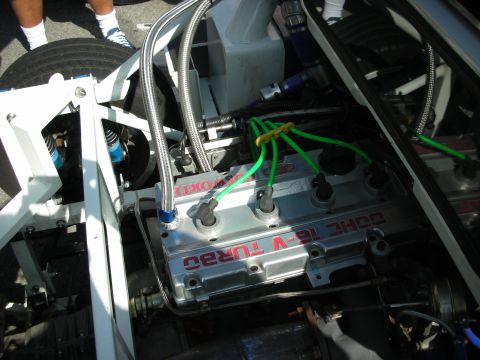1998 Ford Crown Victoria - Close-up of a chromed DOHC 16-valve turbo engine head fitted with braided steel lines and bright green ignition wires in a tube-frame car.