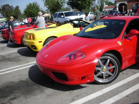1998 Ford Crown Victoria - red Ferrari coupe with the prancing-horse badge leads a row of red and yellow Ferraris parked at a sunny outdoor car meet.