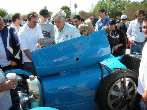 1998 Ford Crown Victoria - Spectators gather around a blue vintage Bugatti grand prix racer as one man lifts the louvered hood panel to view the engine.