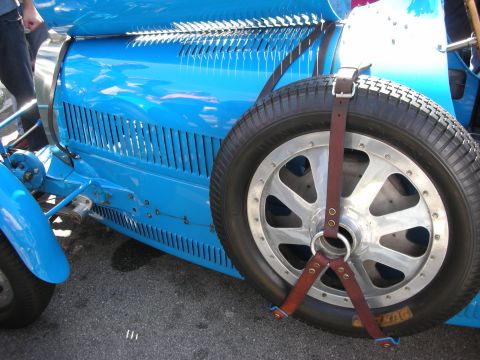 1998 Ford Crown Victoria - louvered blue flank of a vintage Bugatti grand prix car with a spare alloy wheel strapped to the side by leather belts.