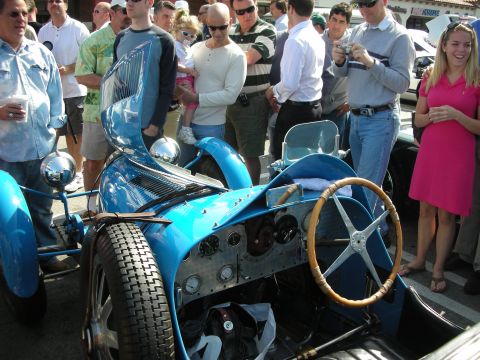 1998 Ford Crown Victoria - Onlookers crowd around a blue vintage Bugatti grand prix racer with its wood-rimmed steering wheel and bare aluminum dash on display.