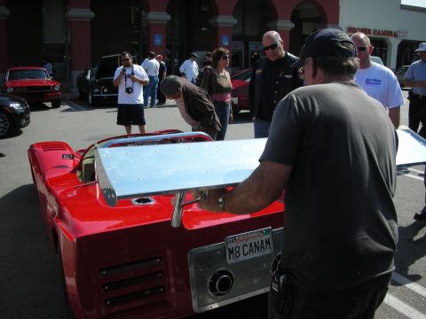 1998 Ford Crown Victoria - man raises the aluminum rear deck of a red Can-Am style racer wearing a California plate reading M8 CANAM at an outdoor car meet.