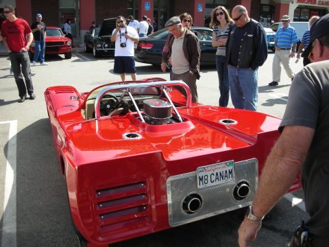 1998 Ford Crown Victoria - Spectators view the rear of a red open-cockpit Can-Am style racer with an exposed V8 and a California plate reading M8 CANAM.
