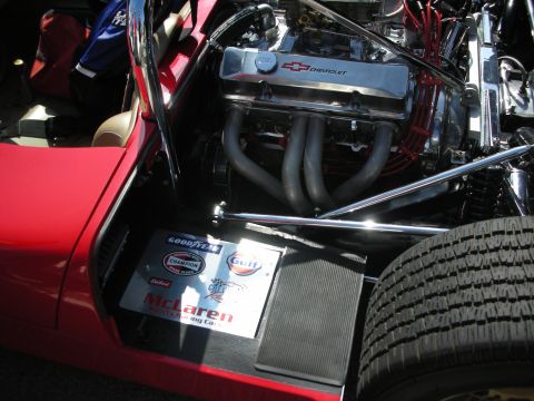 1998 Ford Crown Victoria - Chevrolet V8 with a chrome bowtie valve cover and tubular headers fills the engine bay of a red race car bearing McLaren and Gulf decals.