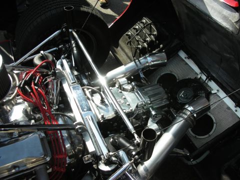 1998 Ford Crown Victoria - highly polished mid-engine bay packed with chrome intake plumbing, headers, red ignition wires and a black mesh panel in a race car.