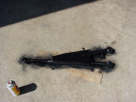 1992 Ford Bronco - A black painted suspension part rests on cardboard on a concrete surface next to a can of spray paint.