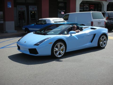 1998 Ford Crown Victoria - light blue Lamborghini Gallardo Spyder convertible cruises top-down through a strip-mall parking lot with the driver visible.