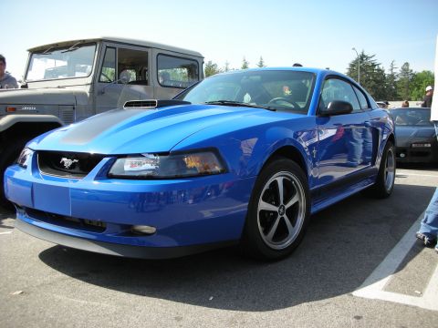 1998 Ford Crown Victoria - blue Ford Mustang Mach 1 coupe with a black shaker hood scoop and five-spoke wheels parked beside a Toyota FJ at a car meet.