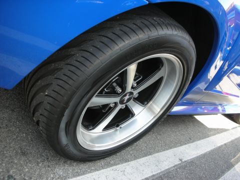 1998 Ford Crown Victoria - Close-up of a polished black-and-machined five-spoke wheel with a pony center cap on a blue Ford Mustang.