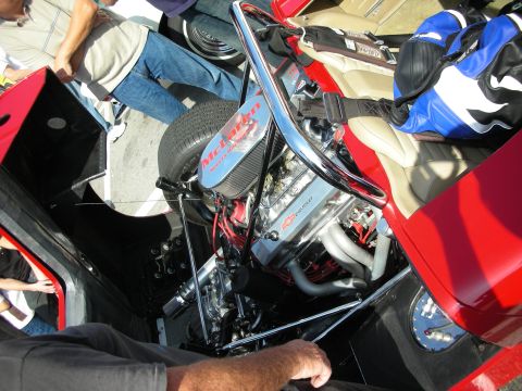 1998 Ford Crown Victoria - mid-mounted V8 topped with a McLaren air cleaner and Chevrolet valve cover sits behind a chrome roll bar in a red open race car.