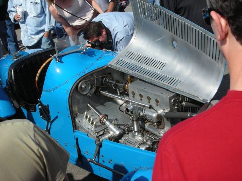 1998 Ford Crown Victoria - Spectators photograph the polished engine and finned aluminum firewall of a light-blue vintage racing car at an outdoor show.