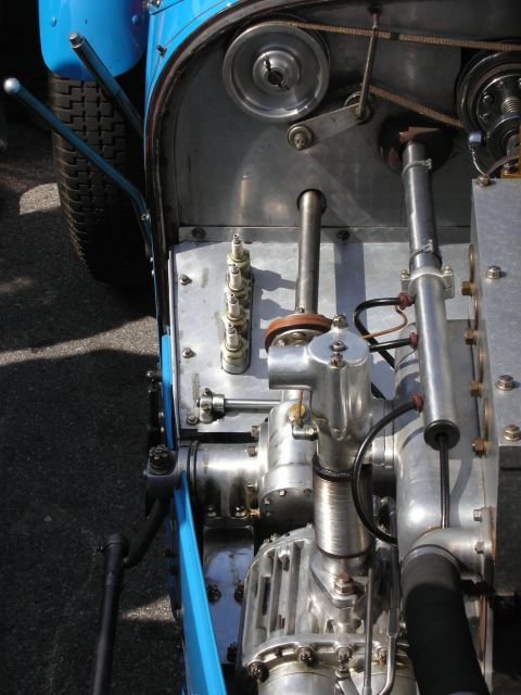 1998 Ford Crown Victoria - Close-up of the exposed inline engine, valve gear and polished linkages alongside the light-blue body of a vintage race car.