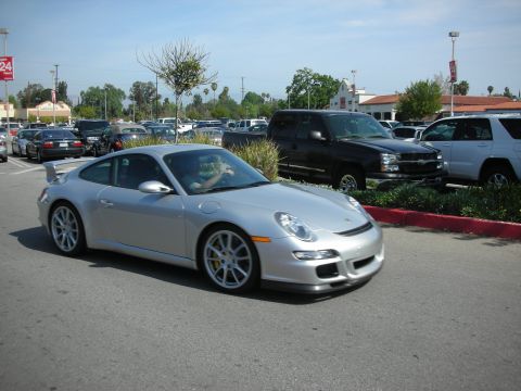 1998 Ford Crown Victoria - silver Porsche 911 GT3 coupe with rear wing and yellow brake calipers drives through a busy parking lot.