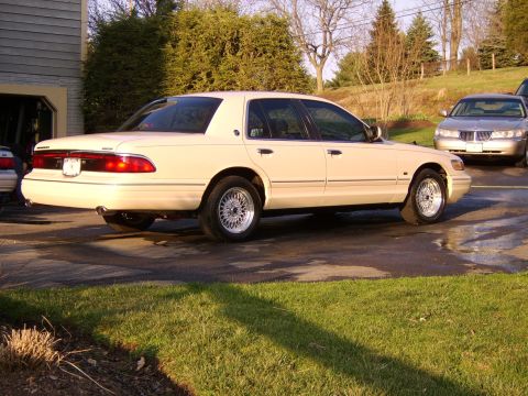 1996 Mercury Grand Marquis - A cream-colored sedan is parked in a driveway with another vehicle visible in the background.