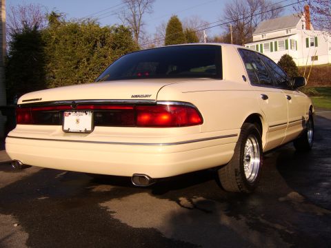 1996 Mercury Grand Marquis - Rear view of a cream-colored 1996 Mercury Grand Marquis parked on a wet driveway.