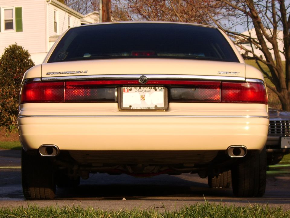 Rear of a cream Mercury Grand Marquis sedan with dual exhaust and Maryland plate, parked on a street.