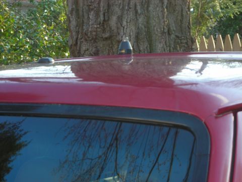 1995 Ford Bronco - Close-up of a red SUV's roof, showing two antennas and reflections.